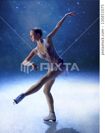 Graceful figure skater extending arm and leg in poised spotlight routine 130851075