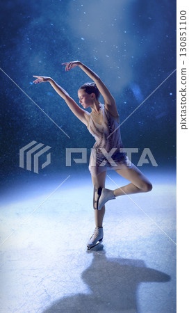 Elegant female figure skater in spotlight performing artistic pose on ice 130851100