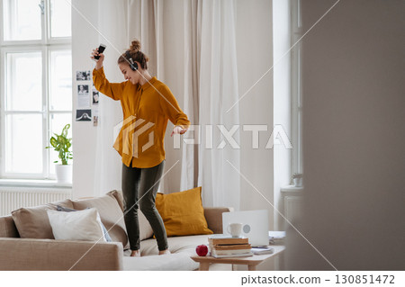 Young woman dancing on sofa with headphones. Young woman dancing on sofa with headphones. 130851472
