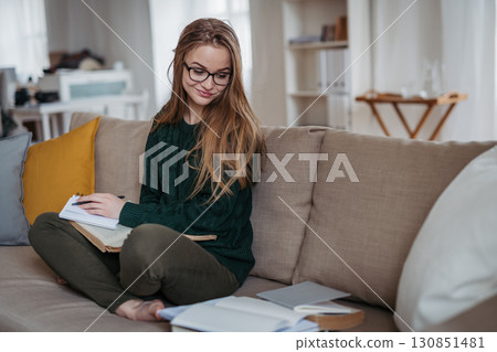 Young female student sitting on sofa and studying. 130851481
