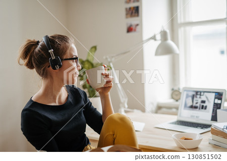 Female student taking break during study session, listening music and drinking coffee. 130851502
