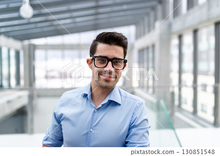 Young businessman standing indoors in an office. Young businessman standing indoors in an office. 130851548