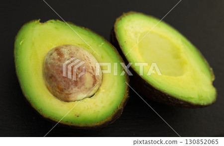Delicious ripe avocado cut in half with pit on black stone board 130852065