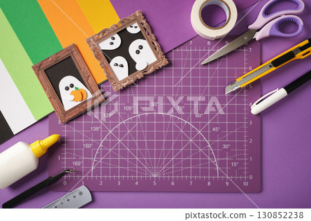 Halloween ghost paper portraits crafts on cutting mat with colorful paper, scissors, glue, knife, tape, marker, ruler. Creative DIY with copyspace 130852238