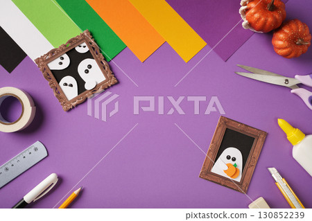 Halloween-themed paper crafts of ghosts in frames on purple background. Copyspace 130852239