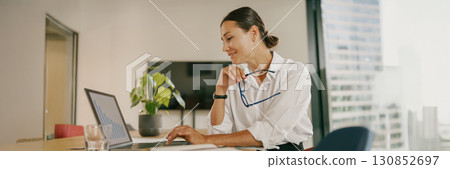 A Professional Woman Diligently Working on Her Laptop in a Contemporary Office Environment 130852697