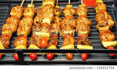 Sizzling skewers of chicken and vegetables grill on an open flame, showcasing the mouthwatering street food experience with juicy meats, vibrant tomatoes, and tangy lemon slices. Street food Sizzling skewers of chicken and vegetables grill on an open flame, showcasing the mouthwatering street food experience with juicy meats, vibrant tomatoes, and tangy lemon slices. Street food 130852738