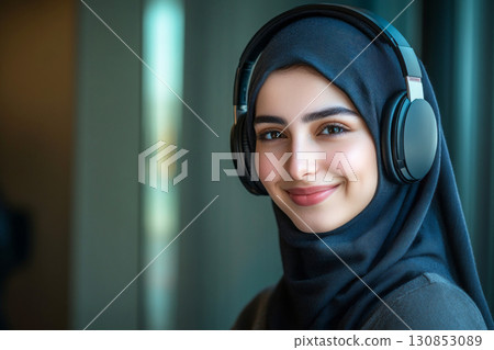 A smiling Arab girl with white headphones on her head stands against a deep green background, showcasing a clean and simple minimalist mock-up design 130853089