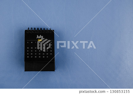 July 2026 black desk calendar on navy blue color leather background. 130853155