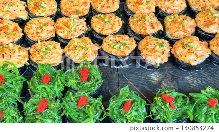 Vibrant display of Asian street food presents spicy tuna rolls with delicate garnishes and seaweed salad topped with bright red caviar, inviting the palette to world of flavors and tradition 130853274