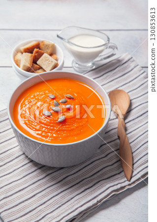 Pumpkin soup-puree with breadcrumbs, cream and seeds on towel, white wooden background 130853613
