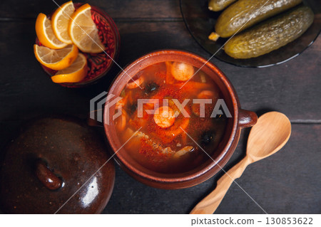 Homemade Traditional Russian soup Solyanka with meat, sausages, vegetables, pickles and olives with lemon in ceramic pot with wooden spoon on dark wooden background Homemade Traditional Russian soup Solyanka with meat, sausages, vegetables, pickles and olives with lemon in ceramic pot with wooden spoon on dark wooden background 130853622