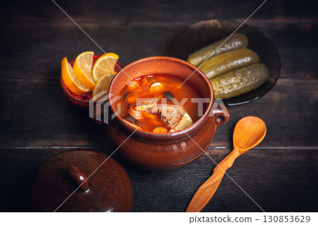 Homemade Traditional Russian soup Solyanka with meat, sausages, vegetables, pickles and olives with lemon in ceramic pot with wooden spoon on dark wooden background Homemade Traditional Russian soup Solyanka with meat, sausages, vegetables, pickles and olives with lemon in ceramic pot with wooden spoon on dark wooden background 130853629