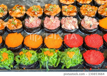 Colorful sushi selection on display, with red tobiko, green seaweed, orange masago, and chopped tuna, inviting street food lovers to enjoy authentic asian flavors Colorful sushi selection on display, with red tobiko, green seaweed, orange masago, and chopped tuna, inviting street food lovers to enjoy authentic asian flavors 130853664