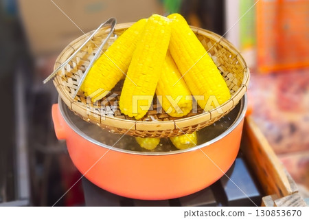 Bright yellow corn cobs steam atop a vibrant orange pot at a street food stall, showcasing a classic and healthy snack. Street food concept 130853670