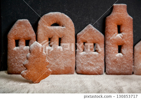Cookie in the form of Christmas tree on the background of gingerbread town sprinkled with powdered sugar Cookie in the form of Christmas tree on the background of gingerbread town sprinkled with powdered sugar 130853717