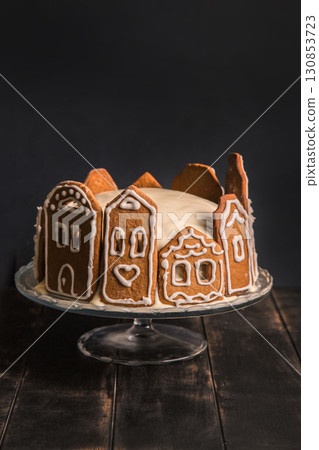 Homemade cake with gingerbread facades of city houses on glass stand and dark wooden table Homemade cake with gingerbread facades of city houses on glass stand and dark wooden table 130853723