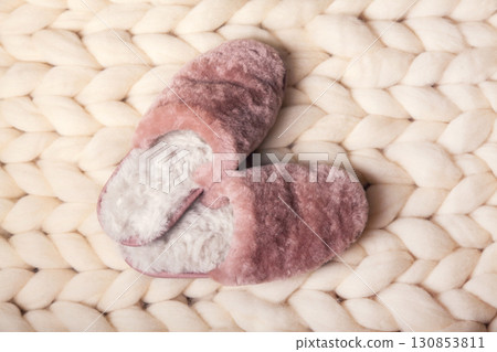 Home slippers made of fur on the background of white merino wool plaid. The atmosphere of homeliness and comfort. Home slippers made of fur on the background of white merino wool plaid. The atmosphere of homeliness and comfort. 130853811