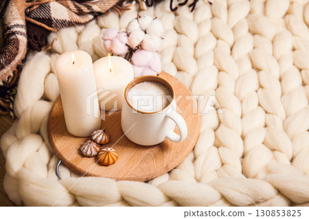 Cup of cappuccino and cookies, candles, checkered plaid on the background of blanket of thick yarn. 130853825