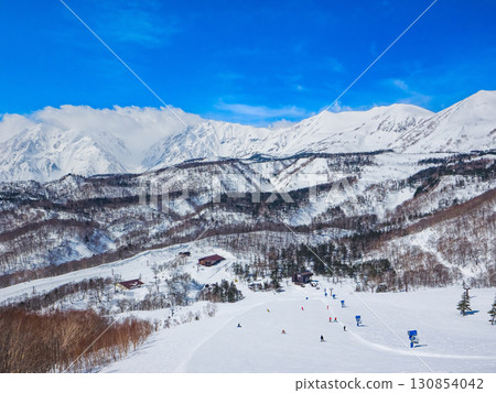 Skiers and snowboarders skiing on the slopes with the Hakuba Sanzan mountains in the background in winter (Hakuba, Tsugaike Kogen, Nagano Prefecture) 130854042