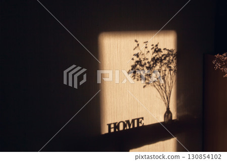 Light and shadow through the window on wall with inscription Home and dried bouquet in transparent vase Light and shadow through the window on wall with inscription Home and dried bouquet in transparent vase 130854102