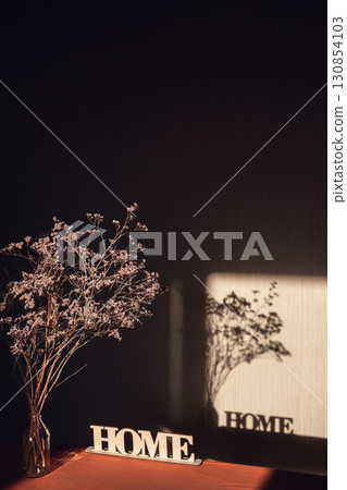 Light and shadow through the window on wall with inscription Home and dried bouquet in transparent vase Light and shadow through the window on wall with inscription Home and dried bouquet in transparent vase 130854103