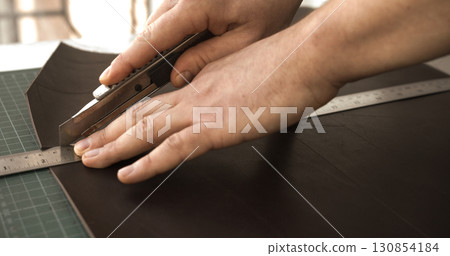 Cutting leather with utility knife and ruler in professional leathercraft workshop Cutting leather with utility knife and ruler in professional leathercraft workshop 130854184