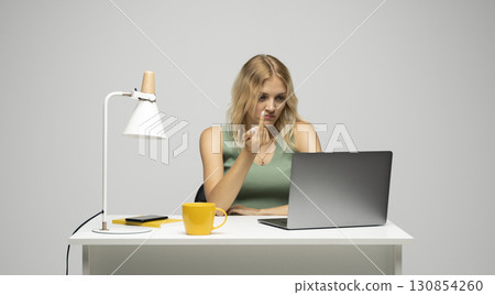 Young blonde woman showing middle finger gesture while sitting with laptop at desk 130854260