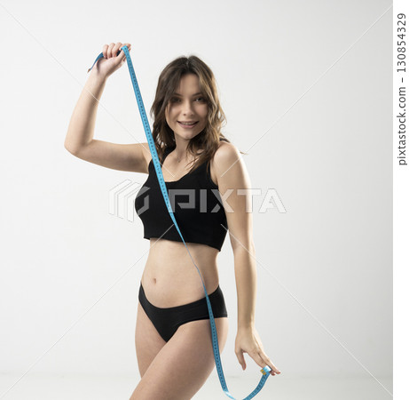 Attractive slim young woman posing with measuring tape in black sportswear indoors Attractive slim young woman posing with measuring tape in black sportswear indoors 130854329