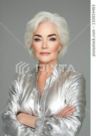 Elegant older woman poses confidently with arms crossed in a silver blouse 130854463