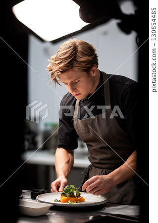 A chef dressed in a white uniform garnishes food with fresh ingredients 130854485