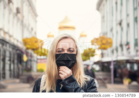 Woman wants to remove a black protective face mask against the background of the city and local attractions - Orthodox Church 130854789