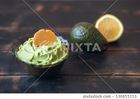 Traditional latinamerican mexican sauce guacamole in bowl with cracker, avocado and lemon on dark background 130855153