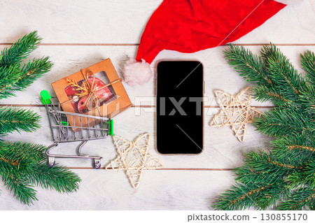Christmas shopping online - small shopping cart with gifts, smartphone and fir branches on wooden background 130855170
