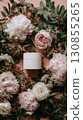 A white cosmetics jar on a bed of soft, lush, pink peonies, roses, and green leaves.  130855265
