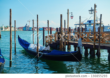 Venetian gondola moored at wooden pier with city waterfront in background Venetian gondola moored at wooden pier with city waterfront in background 130855293