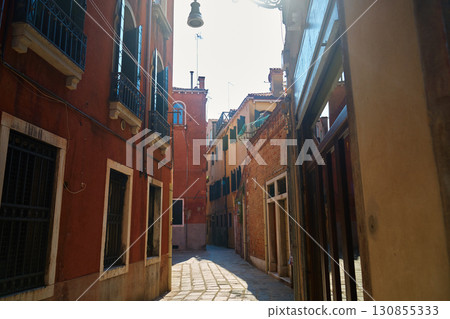 Narrow Venetian alley with historic colorful building facades in sunlight 130855333