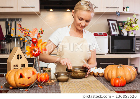 A woman kneads cookie dough for Halloween in the kitchen with autumn decor. A woman kneads cookie dough for Halloween in the kitchen with autumn decor. 130855526
