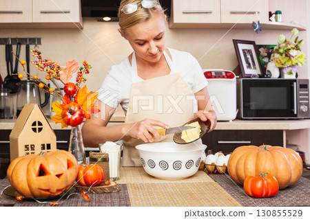 A woman puts butter in the cookie dough for Halloween in the kitchen with autumn decor. A woman puts butter in the cookie dough for Halloween in the kitchen with autumn decor. 130855529