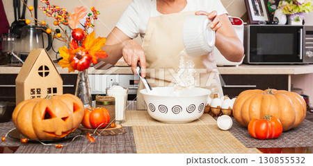 Woman pours flour from glass into cookie dough for Halloween Woman pours flour from glass into cookie dough for Halloween 130855532