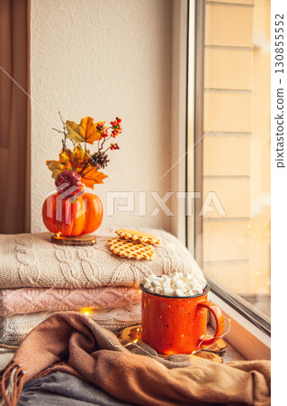 Cozy autumn still life on the windowsill: warm wool sweaters, scarf, pumpkins, maple leaves and a Cup of cocoa with marshmallows and waffles 130855552