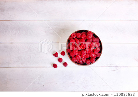 Raspberries in coconut shell bowl on white wooden background Raspberries in coconut shell bowl on white wooden background 130855658