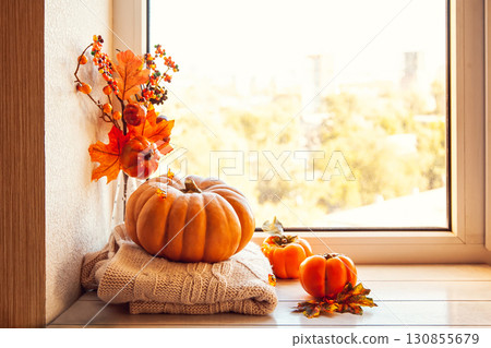 Cozy autumn still life on the windowsill with copy space: pumpkin, warm wool sweaters, maple leaves and persimmon. 130855679