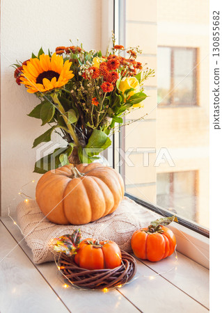 Cozy autumn still life on the windowsill: bouquet with sunflowers, pumpkin, warm wool sweaters and persimmon 130855682