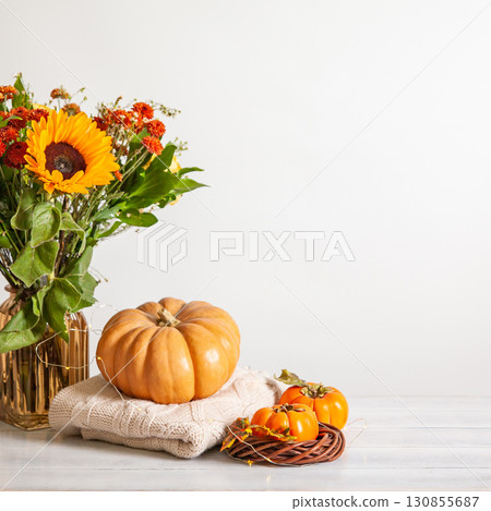 Cozy autumn still life on wooden background with bouquet of sunflowers, pumpkin, sweaters and persimmon 130855687