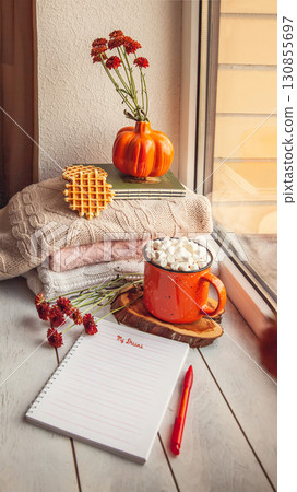 Cozy autumn still life on the windowsill with Notepad for notes: warm wool sweaters, pumpkins, maple leaves and a Cup of cocoa with marshmallows and waffles 130855697