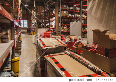 Warehouse interior with stacked boxes and shelves filled with supplies and equipment at midday 130855738