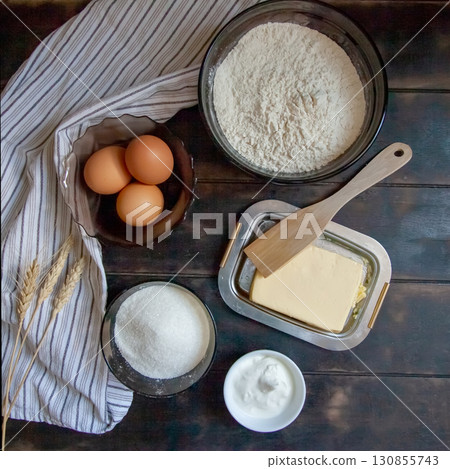 Baking ingredients for shortcrust pastry: butter, flour, eggs, sour cream, a towel on a wooden background. Flatley top view Baking ingredients for shortcrust pastry: butter, flour, eggs, sour cream, a towel on a wooden background. Flatley top view 130855743