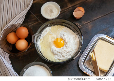 Baking ingredients for shortcrust pastry: butter, flour, eggs, sour cream, a towel on a wooden background. Flatley top view Baking ingredients for shortcrust pastry: butter, flour, eggs, sour cream, a towel on a wooden background. Flatley top view 130855748