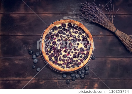 Rustic shortbread pie with blueberries in sour cream filling on a wooden background and a bouquet of dried lavender. Flatley top view. 130855754